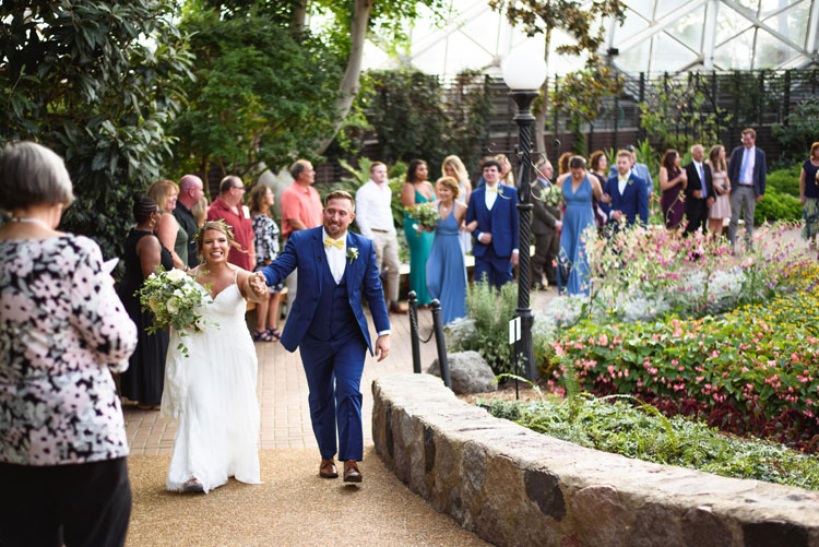 Bride and groom holding hands while walking back up the isle after their ceremony in The Domes.