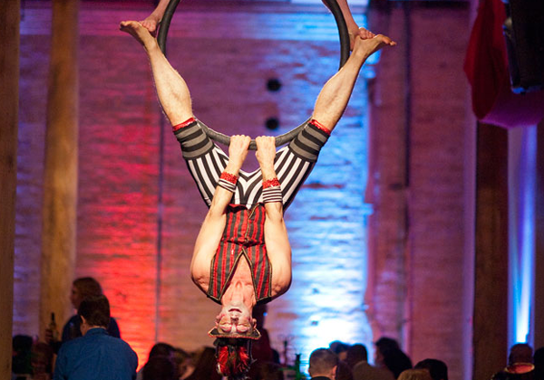 Acrobat hanging upside down from a ring.