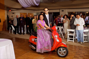 Bride and groom posing while the bride sits on a red moped.