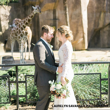 Bride and groom with a giraffe in the background at Milwaukee County Zoo.