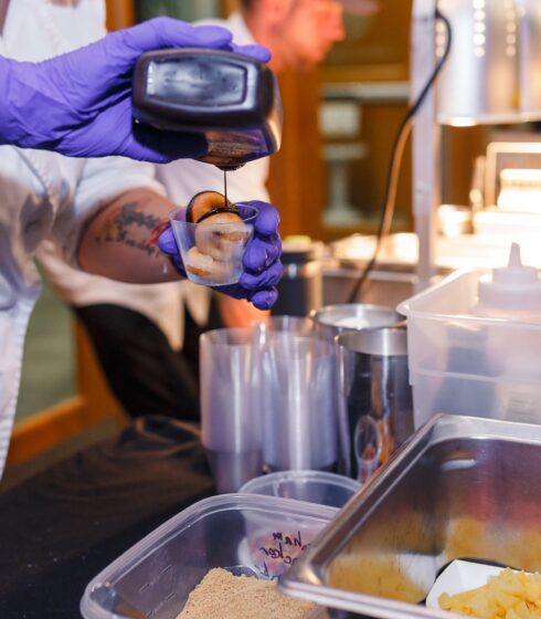 A chef pouring chocolate over mini donuts.