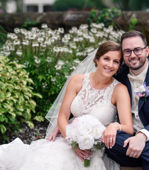 Bride and groom sitting together and smiling at the camera with pretty bushes in the background.