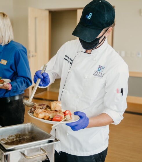 Chef pouring gravy on a plate of food they are serving.