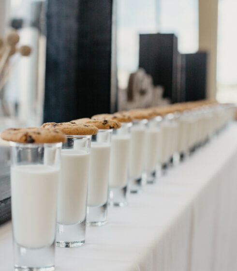 Glasses of milk with cookies on top lined up in a row.