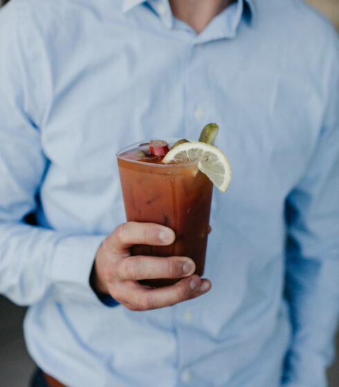 A man in a blue button down shirt holding a bloody mary.