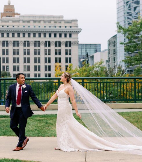 A bride and groom holding hands while the brides veil flows out behind her.