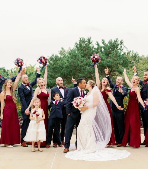 Bride and groom kissing while the wedding party celebrates behind them.