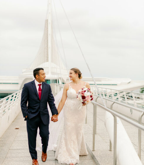 Bride and groom holding hands while walking on the bridge in front of the Milwaukee Art Museum.