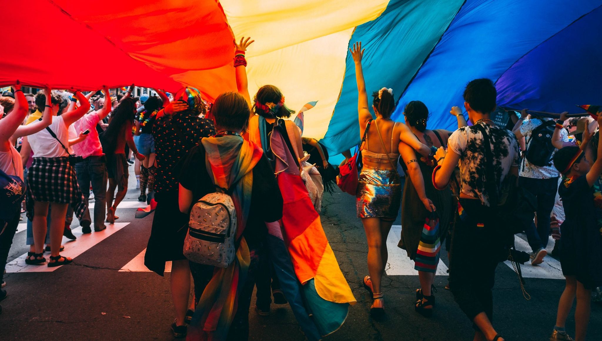 People walking under a pride flag during a parade