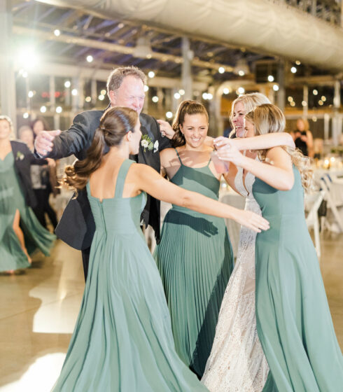 Father embracing bride and bridesmaids on dance floor.