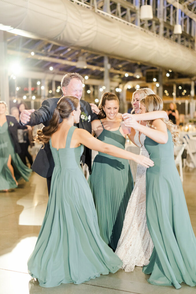 Father embracing bride and bridesmaids on dance floor.