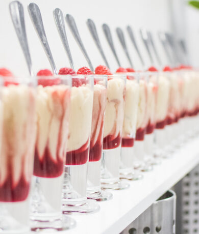 several vanilla and raspberry desserts lined up in glass cups